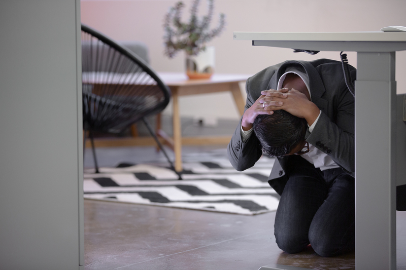 A man doing Drop Cover Hold under a work desk
